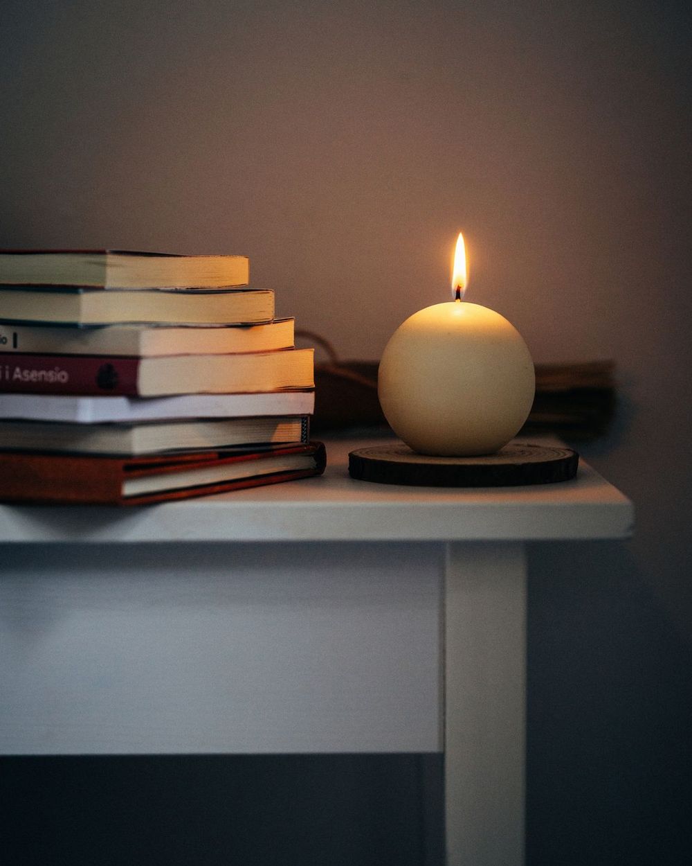Una vela encendida junto a una pila de libros sobre una mesita